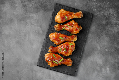 Roasted Baked chicken legs drumsticks on black slate board on dark background. Meal, dinner diet concept, diet. Copy space for text.