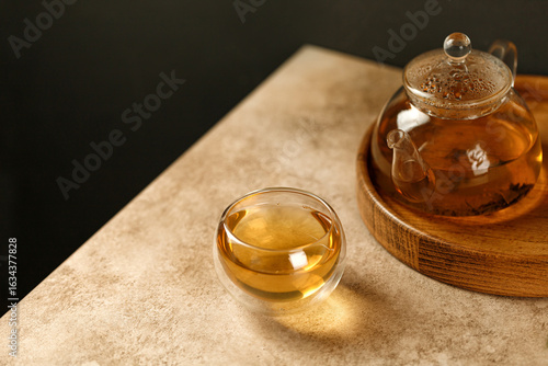 Double Wall Glass Cup with green herbal tea and glass teapot on wood tray and beige background