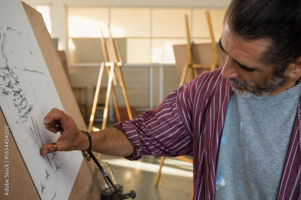 Obraz premium Artist is smudging charcoal sketch on drawing board on easel in art studio under window light