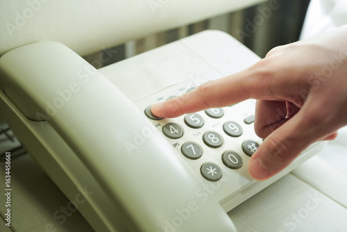 A young woman making a call using a landline phone in a hotel room