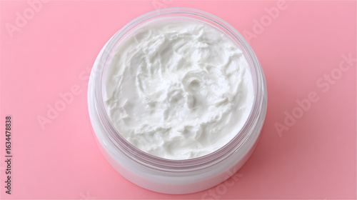 Top view of a white beauty cream in an open jar on a pink background. High-quality skincare product texture, symbolizing self-care, spa and cosmetic concepts