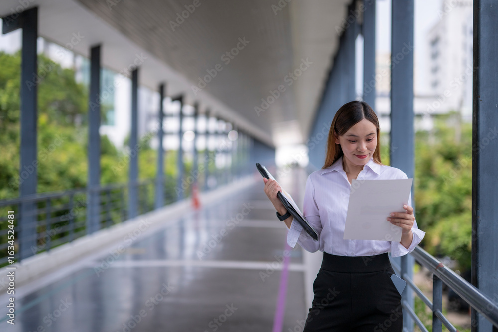 Fototapeta premium Businesswoman reading documents and holding laptop in covered walkway
