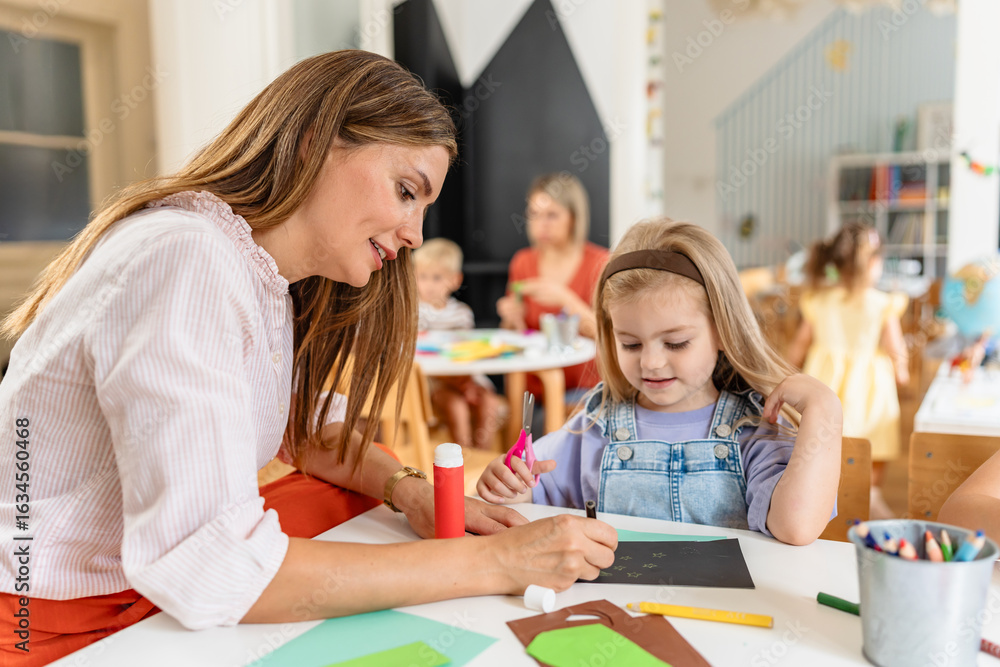 Fototapeta premium Preschool teacher guiding children from diverse backgrounds during a colorful arts and crafts activity in a bright classroom.