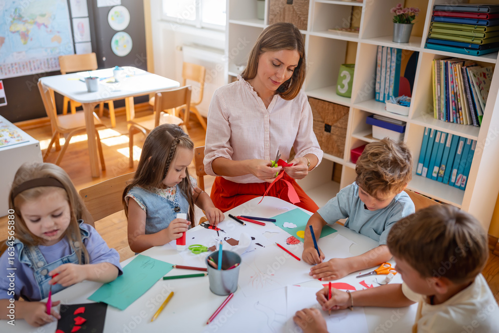 Fototapeta premium Preschool teacher guiding children from diverse backgrounds during a colorful arts and crafts activity in a bright classroom.