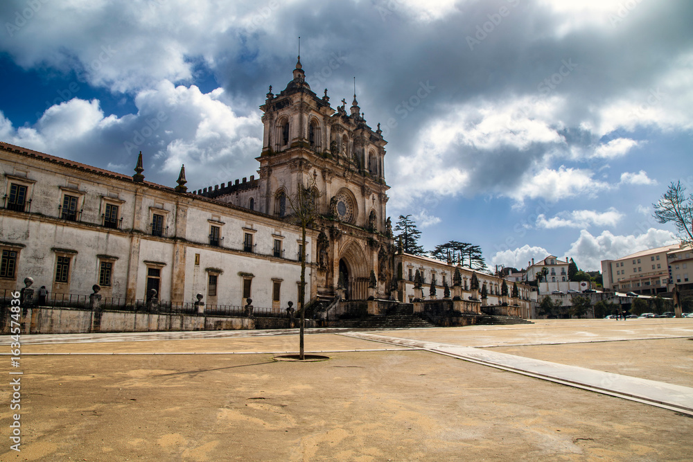 Obraz premium The grand and majestic facade of the Monastery of Santa Maria de Alcobaça on a sunny day, showcasing its impressive architecture and wide courtyard in Alcobaça, Portugal.