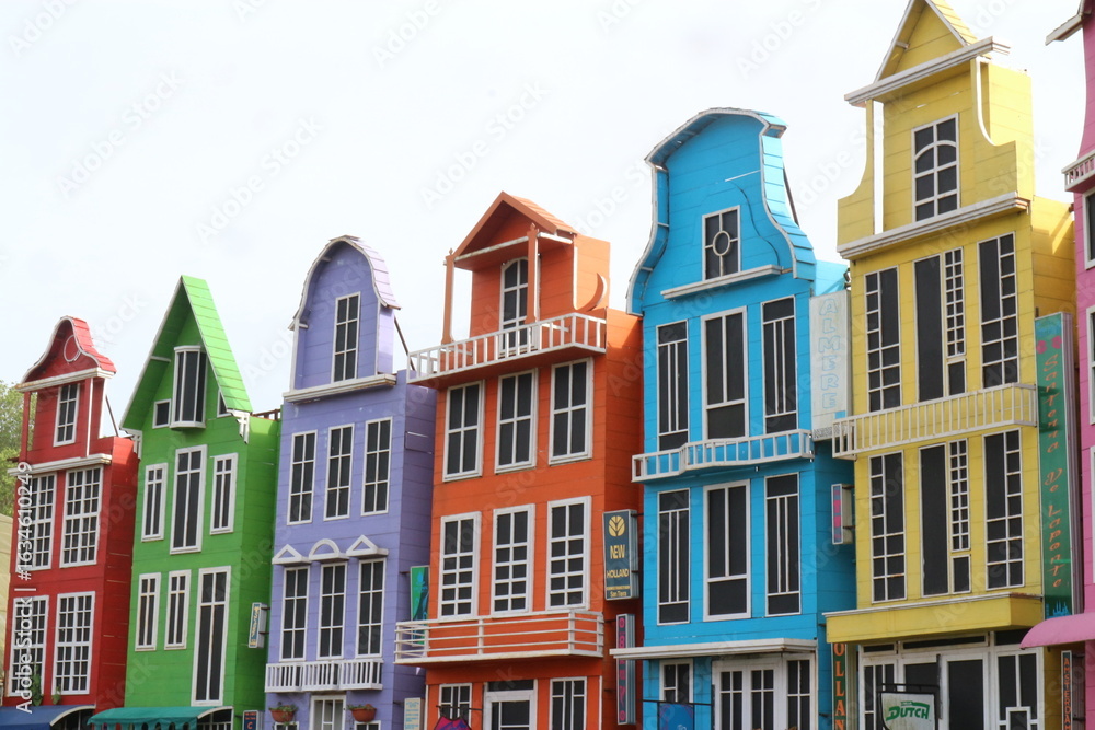 Fototapeta premium Row of Colorful Buildings in Bright Hues A picturesque row of buildings painted in vivid colors including purple, orange, and yellow, perfect for travel and design concepts.
