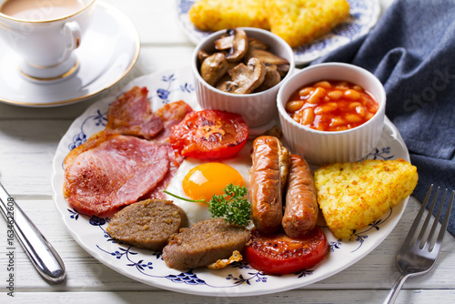 Full Irish or English breakfast with sausages, bacon, pudding, fried egg with runny yolk, hash browns, beans and tomatoes