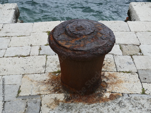 Foto Rusty old metal mooring bollard on stone dock by the ocean