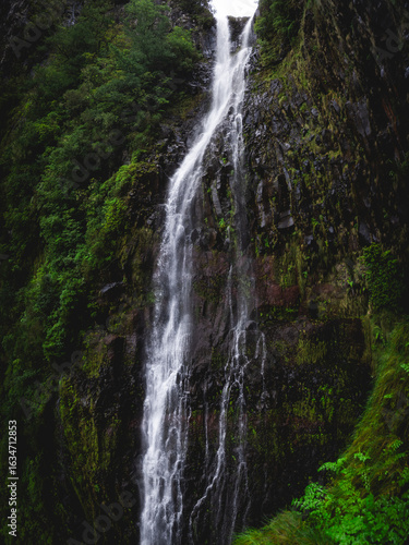 The powerful Risco Waterfall cascading down a rocky cliff face in the lush green laurel forest of Madeira, Portugal