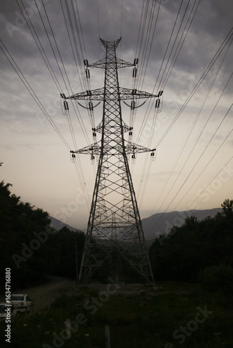 Fotografie Tall lattice transmission pylon carrying multiple high‑voltage lines across a valley at dusk