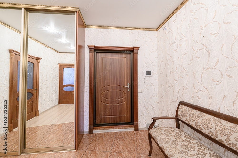 Fototapeta premium hallway with tiled floor, floral wallpaper, and wooden furniture. There's a mirrored closet, a wooden door, and a bench. The style looks classic and cozy