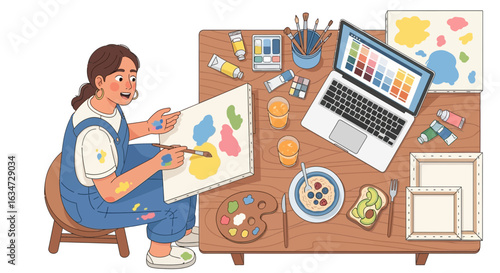 Creative artist painting at her desk while enjoying breakfast and using a laptop