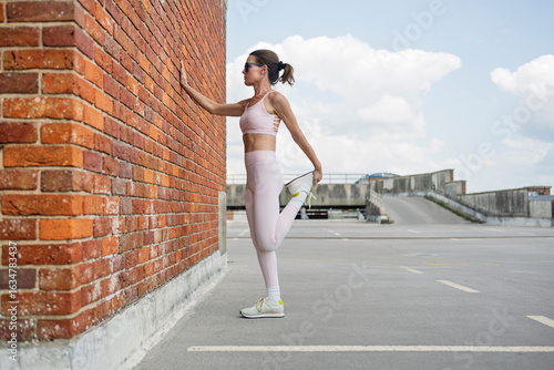fit sporty woman doing stretching exercises in urban setting, brick wall.