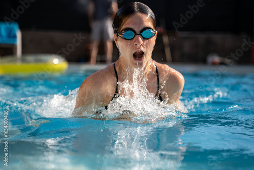 Canvas Print Young woman swimming breaststroke style in outdoor pool, athletic summer training in clear blue water