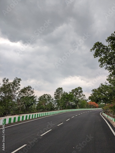 Image of the road from Thotlakonda Stupa to Beach, down the hill, with view of clean road, sea, clouds and vegetation, in the Vizag city of Andhra Pradesh. It shows the coastal area of Bay of Bengal.