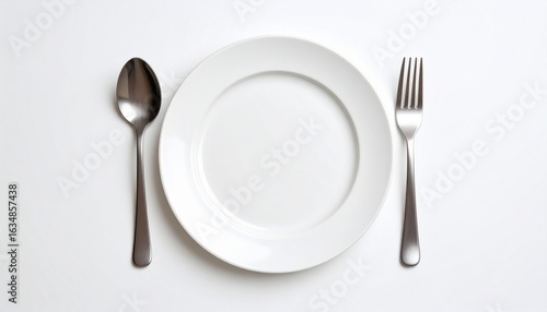 Minimalist table setting with white plate, spoon, and fork on white background.