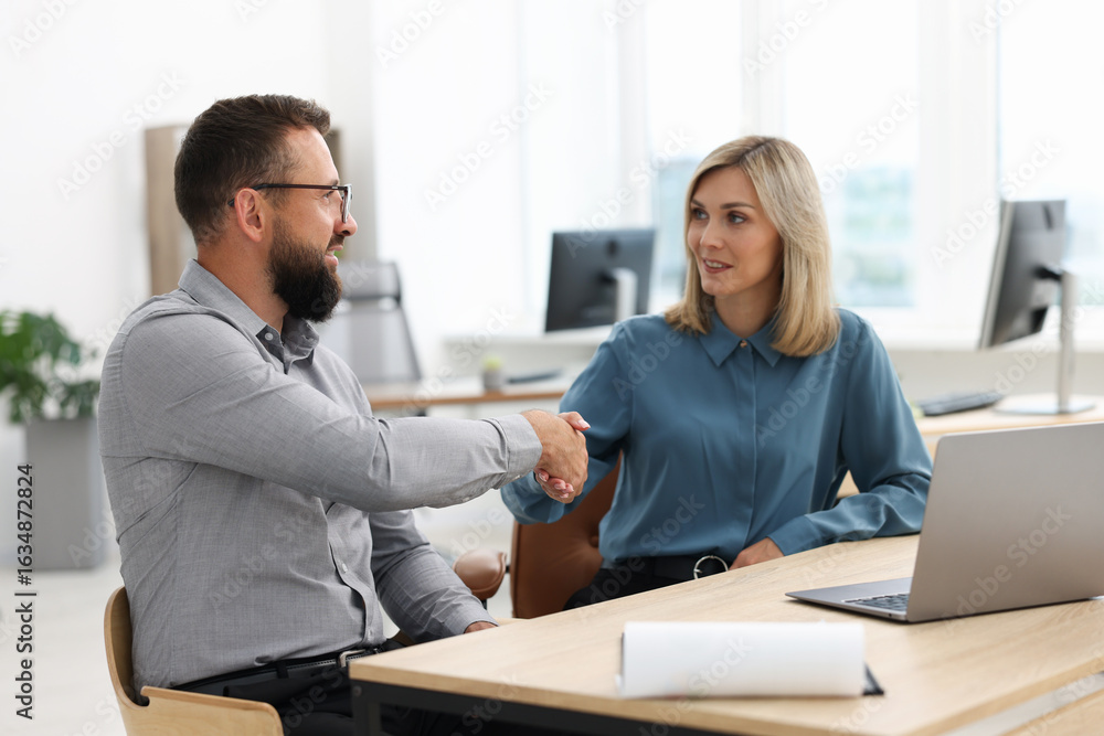 Smiling business partners shaking hands at table in office Smiling business partners shaking hands at table in office