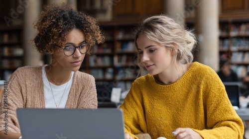 two women sitting at a table with a laptop
