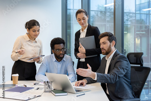 A group of diverse professionals is discussing work at an office desk, actively engaging and focusing on their collaborative tasks.