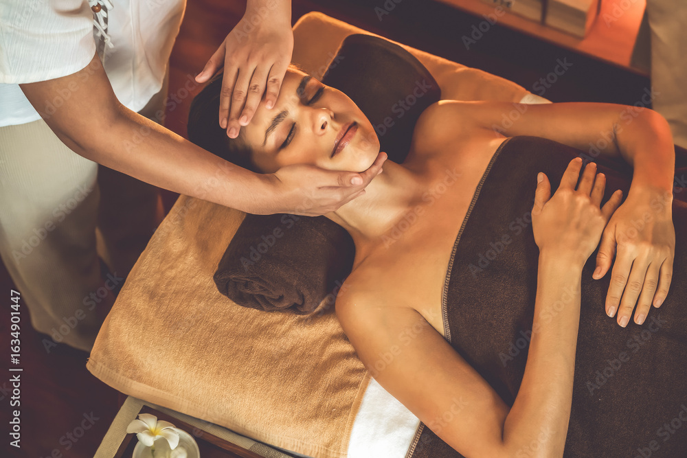 Obraz premium Caucasian woman enjoying relaxing anti-stress head massage and pampering facial beauty skin recreation leisure in warm candle lighting ambient salon spa in luxury resort or hotel. Quiescent