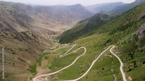 Aerial drone view of Teskey-Torpok Pass (38 Parrots), 3,138 m above sea level in Kyrgyzstan’s Tien Shan mountains, with a winding dirt road running down the slope.