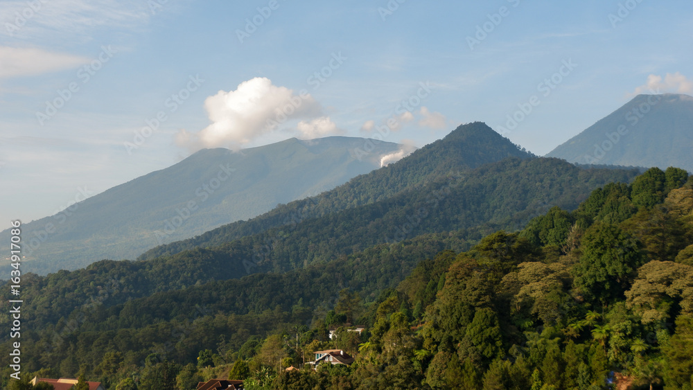 Fototapeta premium Mountains landscape. Panorama of beautiful countryside of Indonesia in sunny afternoon. landscape in tropical. Grassy field and rolling hills. rural scenery with blue sky and trees. Idyllic mountain.