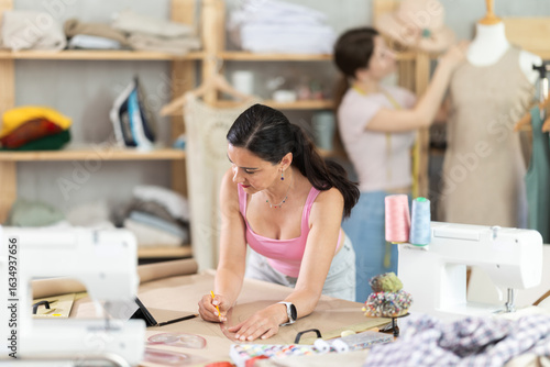 Foto Experienced female tailor drawing clothing outlines on paper in sewing studio