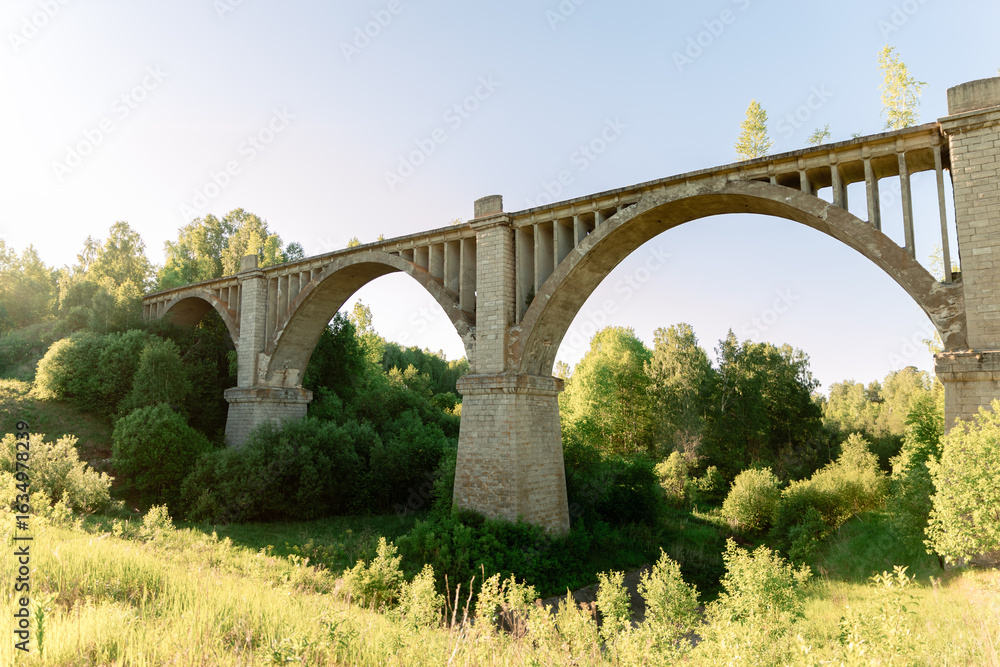 Fototapeta premium A viaduct with stone arches against a bright blue sky at sunset. Old stone bridge in the countryside