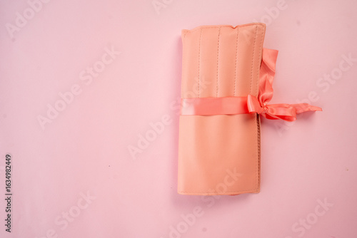 фотографія closed beige makeup brush case tied with pink ribbon rests on pink background