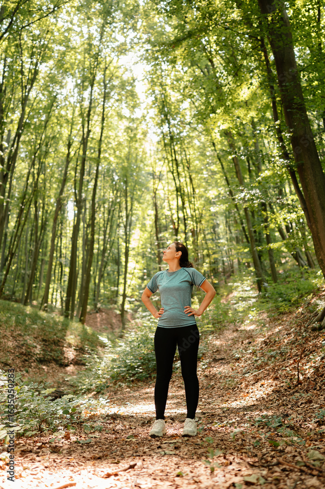 Obraz premium A woman stands confidently in the vibrant green forest, fully enjoying the tranquility of nature around her