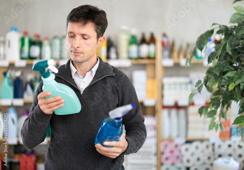 Tableau sur toile Attentive man in his middle ages reviewing cleaning sprays to buy at supermarket