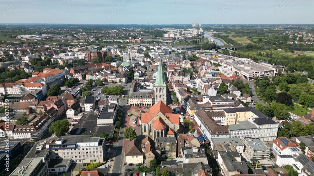Fototapeta premium Aerial view of a European city with red-roofed buildings, a historic church, residential areas, and green surroundings. Ideal for urban, editorial, or architectural use.