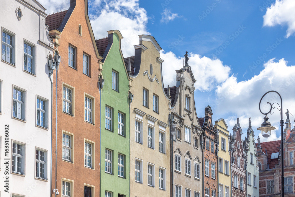 Fototapeta premium Gdansk, a city on the Baltic coast of northern Poland, Europe. Colorful historic buildings line the street, each with unique architectural details and hues against a bright blue sky with fluffy clouds