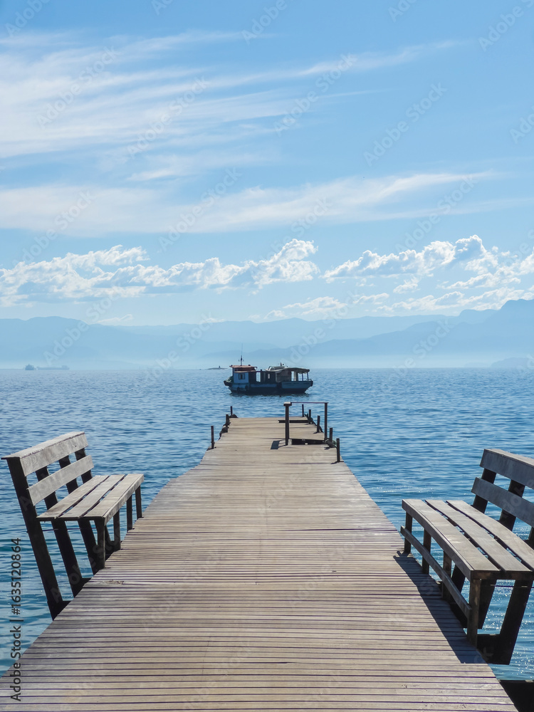 Obraz premium Wooden Pier with Benches and Boat in the Distance in Ilha Grande, Brazil
