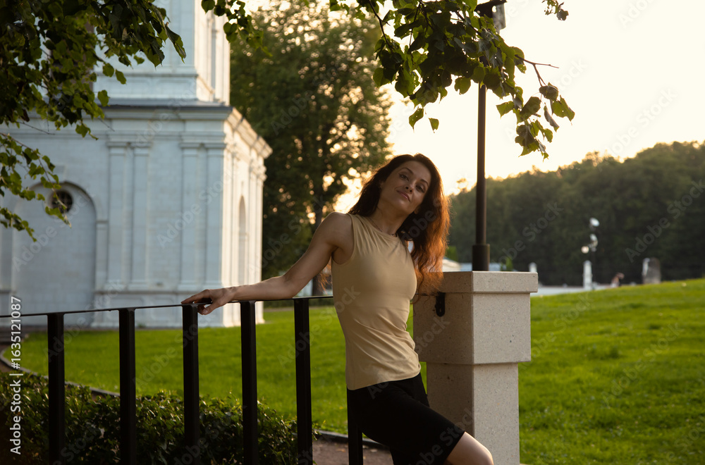 Naklejka premium Beauty happy face woman, enjoying fresh air standing under the tree in a city street park at white column. Female brunette model relax in summer day with smiling face with long brown hair.