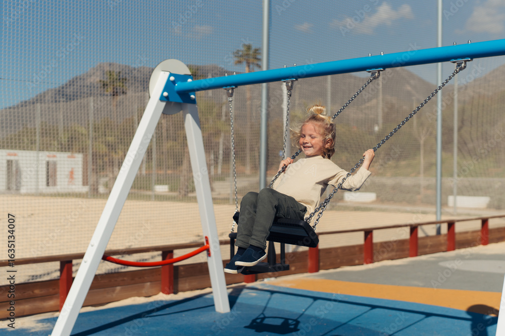 Naklejka premium A young girl swinging happily at the playground, her feet reaching high in the air while enjoying a moment of playful freedom. She gazes ahead with a calm expression