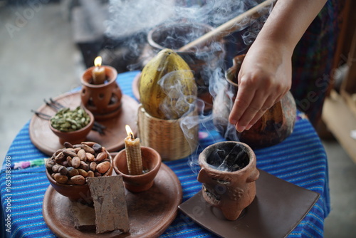 Various Guatemalan Mayan ingredientes on a table decorated with Mayan textile like cacao beans, vanilla beans, cacao pods, beeswax candles, cardamom.