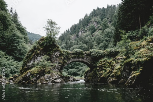 Aged stone arch bridge spanning a mossy, rocky river gorge, lush green forest slopes rise above