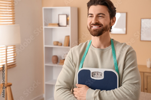 Young man with weight scales and tape measure at home