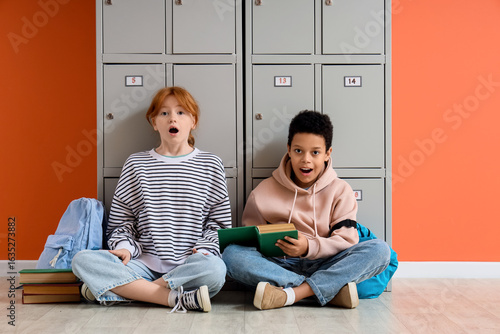Surprised teenage students reading book near locker at school