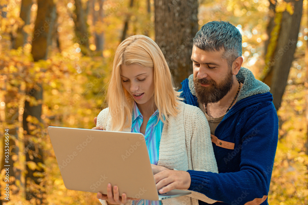 Naklejka premium Business couple, man and woman using laptop in Autumn fall nature park. Business outdoor in autumn park. Couple in Autumn fall park. Man and woman near Autumn fall leaves.