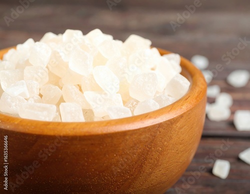 a pile of sugar in a bowl, with sugar grains scattered on the table.