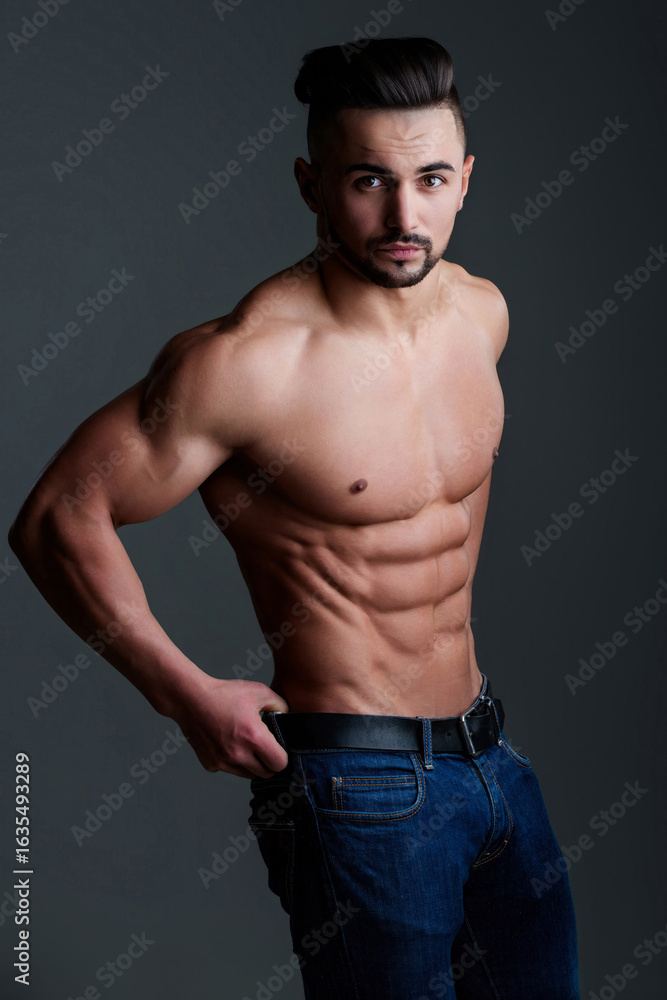 Fototapeta premium Slim muscular male model at black background. Fitness shirtless guy in posing in studio. Man with six pack abs. Brutal sexy man with six pack abs, fitness male model. Muscled guy.