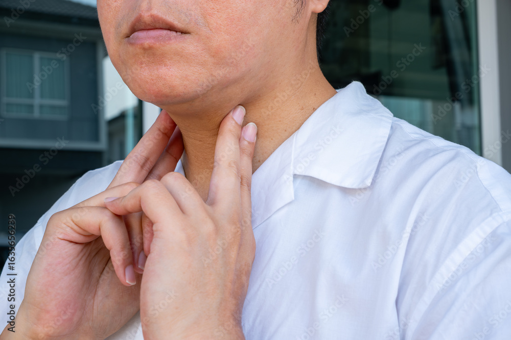 Fototapeta premium Close-up of hand pressing sore throat against a blurred background, illustrating tracheal discomfort and respiratory distress. Ideal for throat and airway treatment ads.