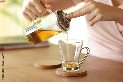 Woman hand pouring tea from infuser in a glass