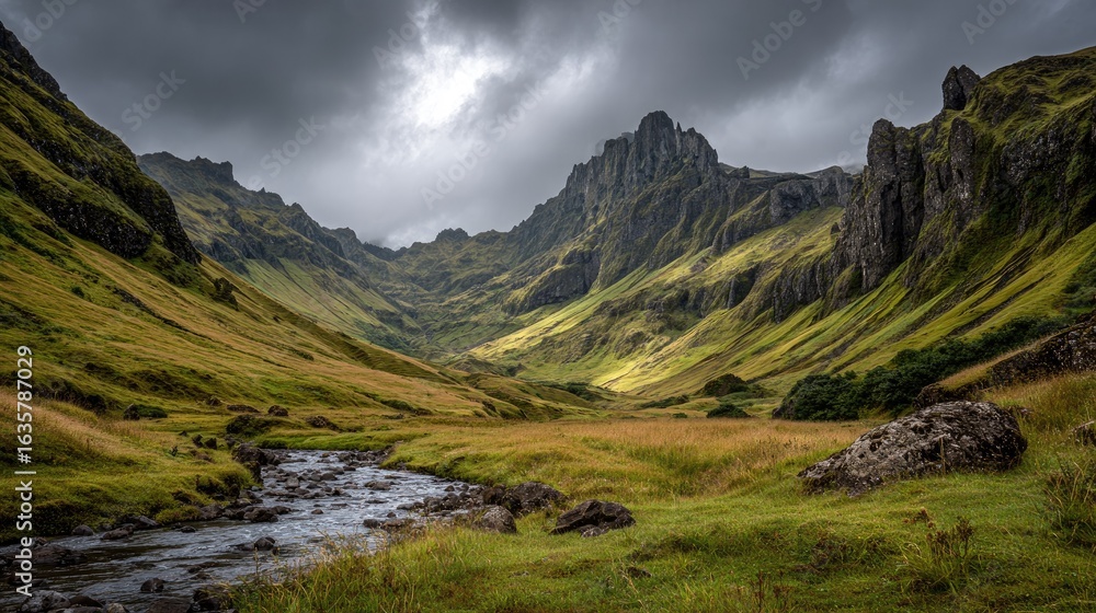 Naklejka premium Sunlit valley with a stream, dramatic mountains and cloudy sky