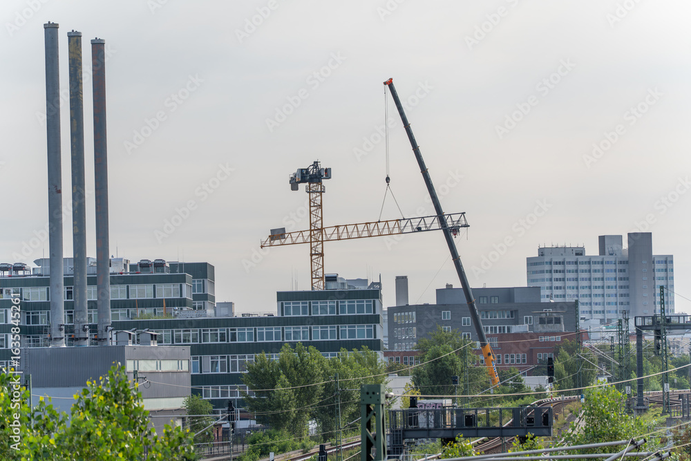 Fototapeta premium A crane raises a boom arm over modern office and industrial buildings. The scene depicts urban change with new buildings and construction activities.