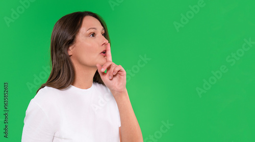 Woman holding her finger to her lips while standing against a green background, signaling for silence in a quiet and calm atmosphere