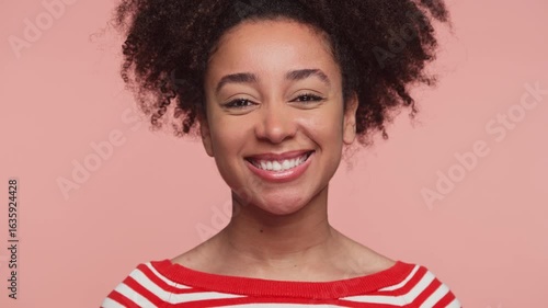 Smiling woman winking playfully at camera on pink background