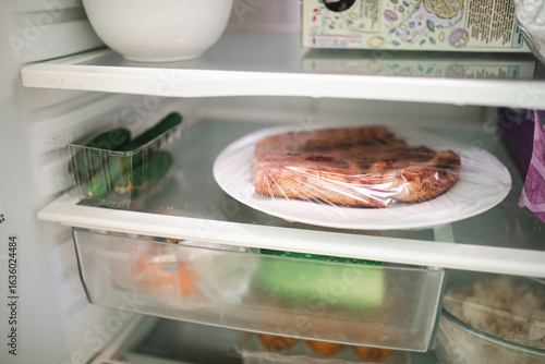 Obraz na plátně Plate of leftover sausages on shelf of fridge surrounded by vegetables